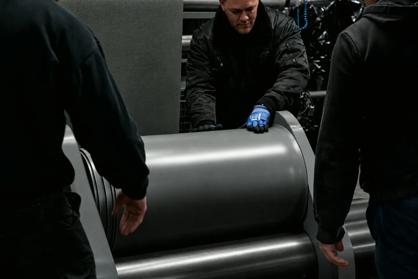 Three people handling a roll of matting off the line at the factory